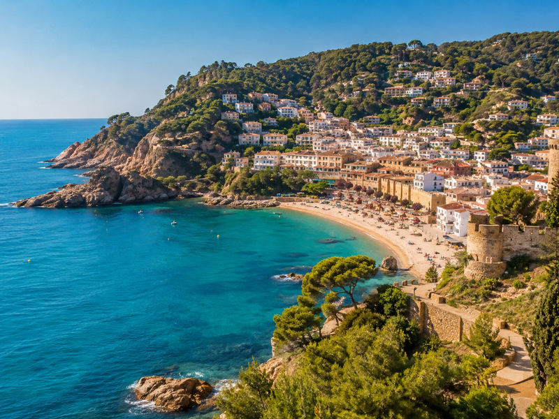 Vista panorámica de una localidad costera de la Costa Brava con viviendas en la ladera, playa, mar Mediterráneo y torres de piedra