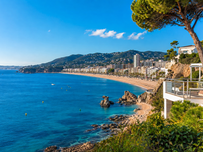 Vista mediterránea de Lloret de Mar con playa, edificios residenciales y viviendas en la ladera, representativa del mercado de compra y alquiler de pisos.